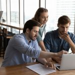 three people sitting around a computer.